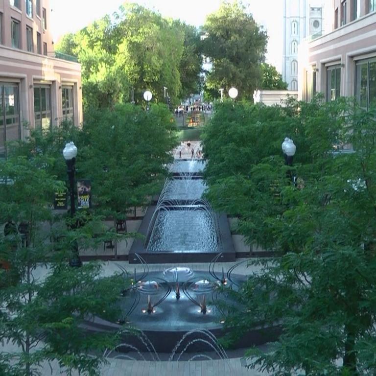Ein großer, grüner Stadtplatz mit einem gestuften Wasserbecken und umgebenden historischen Gebäuden.