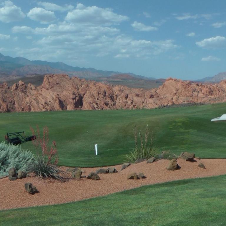 Panoramablick auf einen Golfplatz mit grünem Rasen, Sandbunker und einer weiten Bergkulisse.