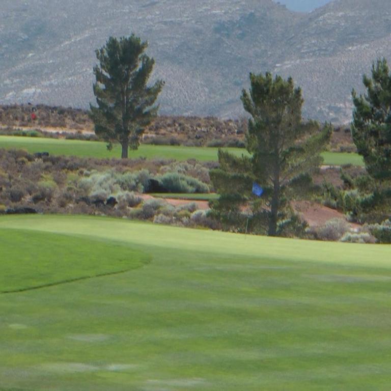 Eine Ansicht eines gepflegten Golfplatzes, der vor einer Kulisse aus trockenen, bewaldeten Hügeln liegt.
