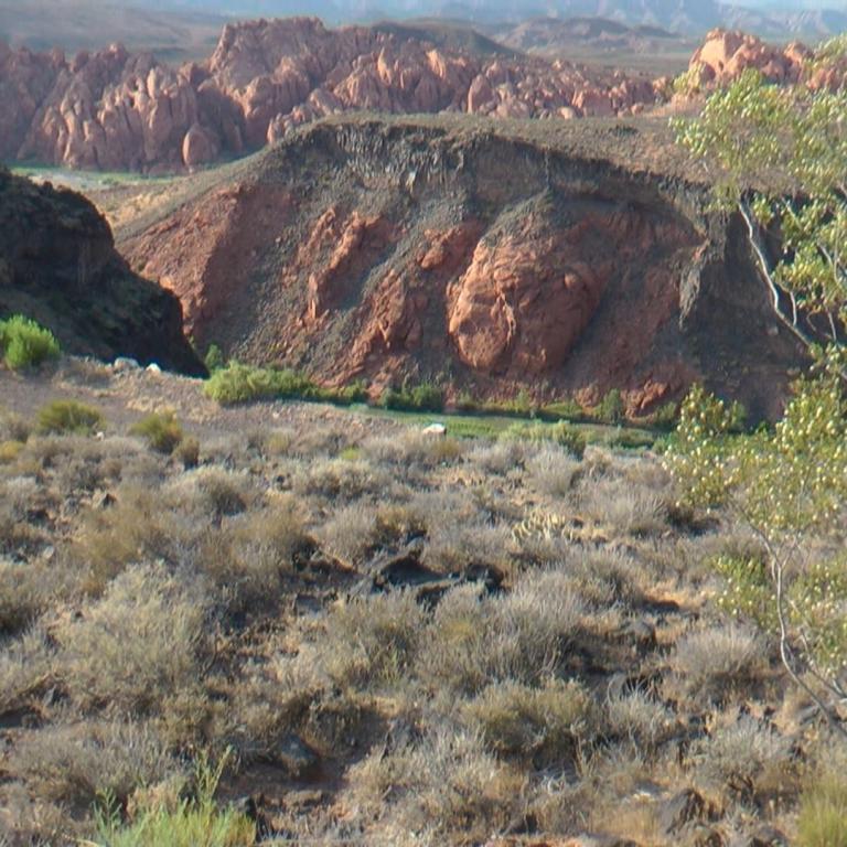 Arides Landschaftsbild mit einem trockenen Vordergrund, steilen, ockerfarbenen Hügeln und einer Bergkette im Hintergrund.