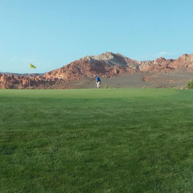 Ein Golfplatz mit grünem Rasen im Vordergrund und einer beeindruckenden Bergkette im Hintergrund.