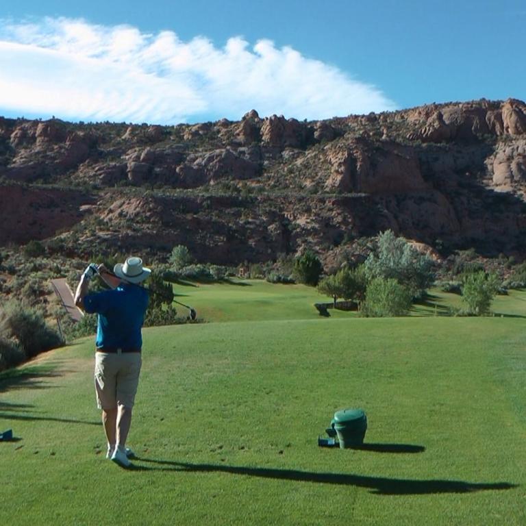 Ein Golfer schlägt einen Ball vor der Kulisse einer großen, felsigen Bergkette.